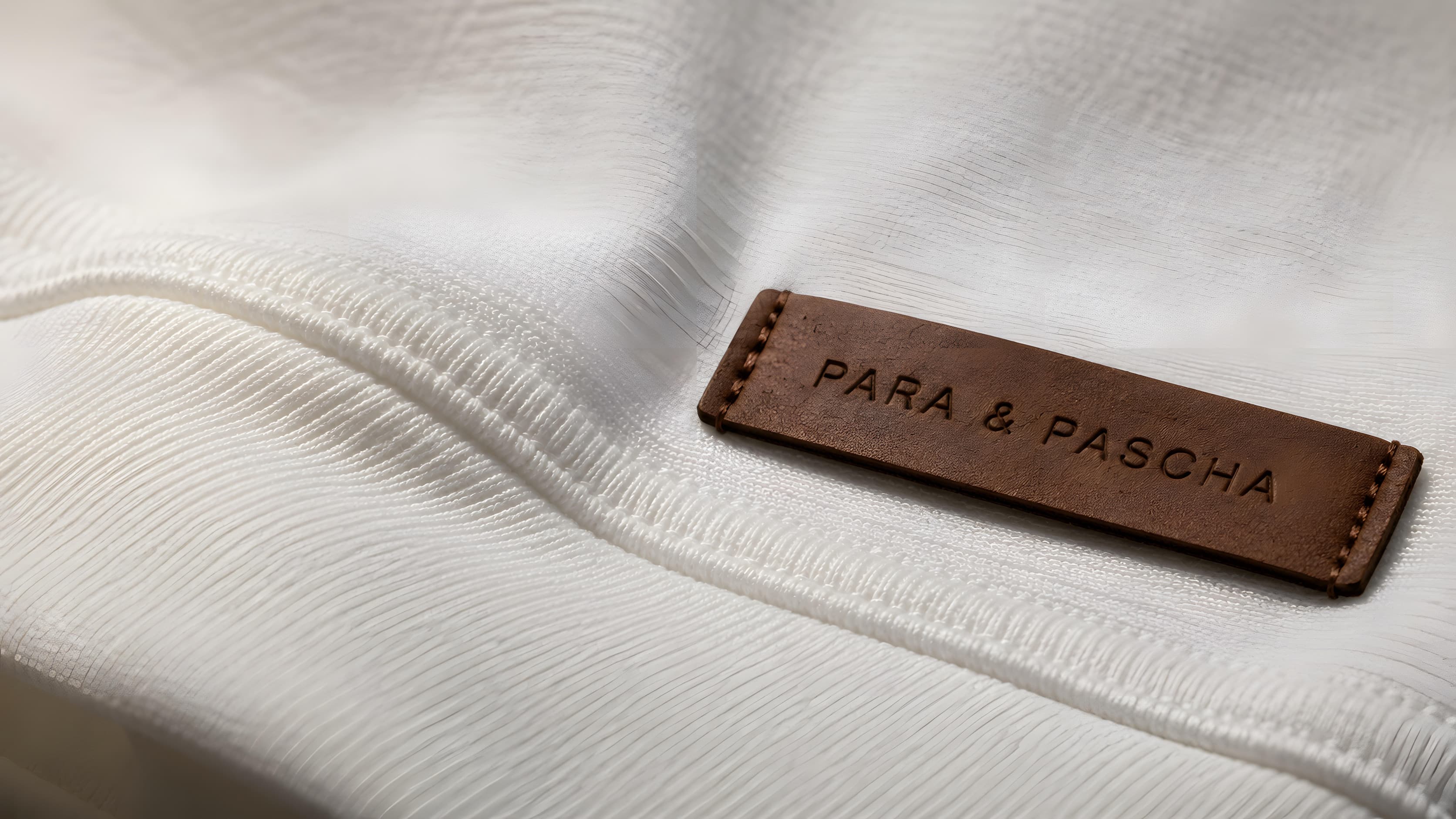 PARA & PASCHA heavyweight cotton at macro scale, the leather plaque stitched into the seam.